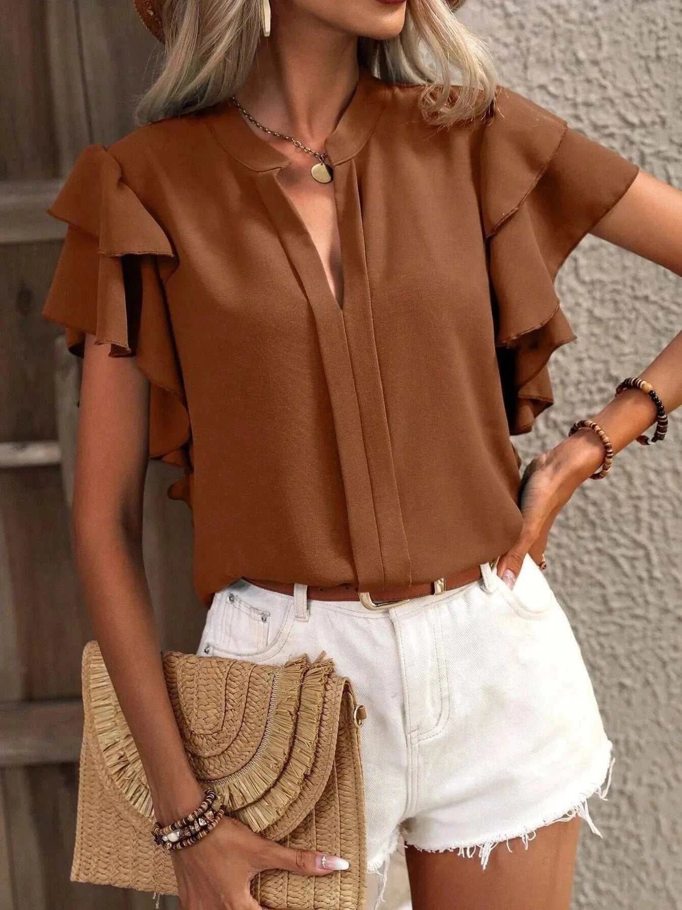 Brown ruffle sleeve notched blouse made of 100% polyester paired with white shorts and a woven clutch bag.