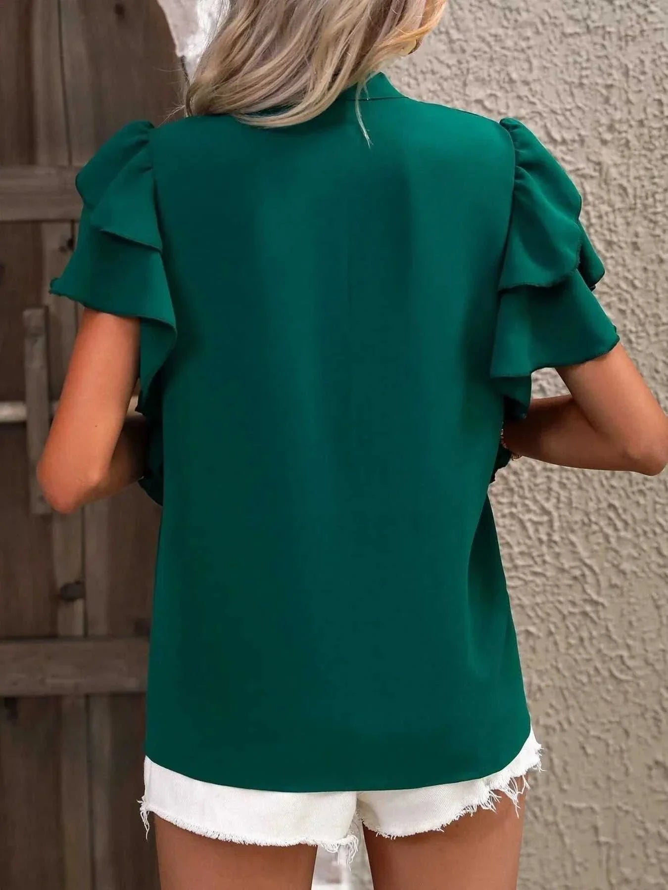 Green ruffle sleeve notched blouse worn with white shorts, shown from the back.