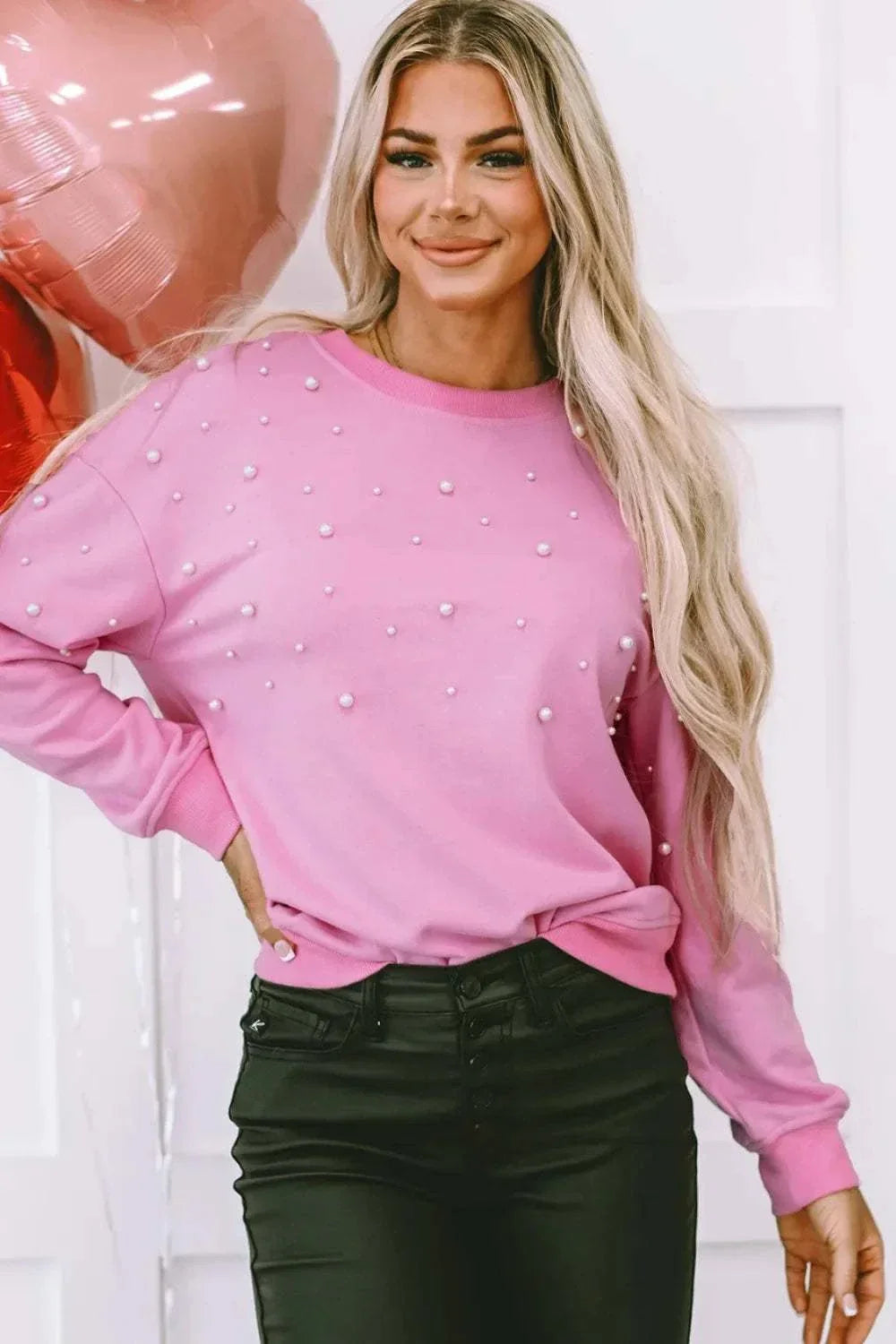 Woman wearing pink pearl round neck dropped shoulder sweatshirt with long sleeves and black pants