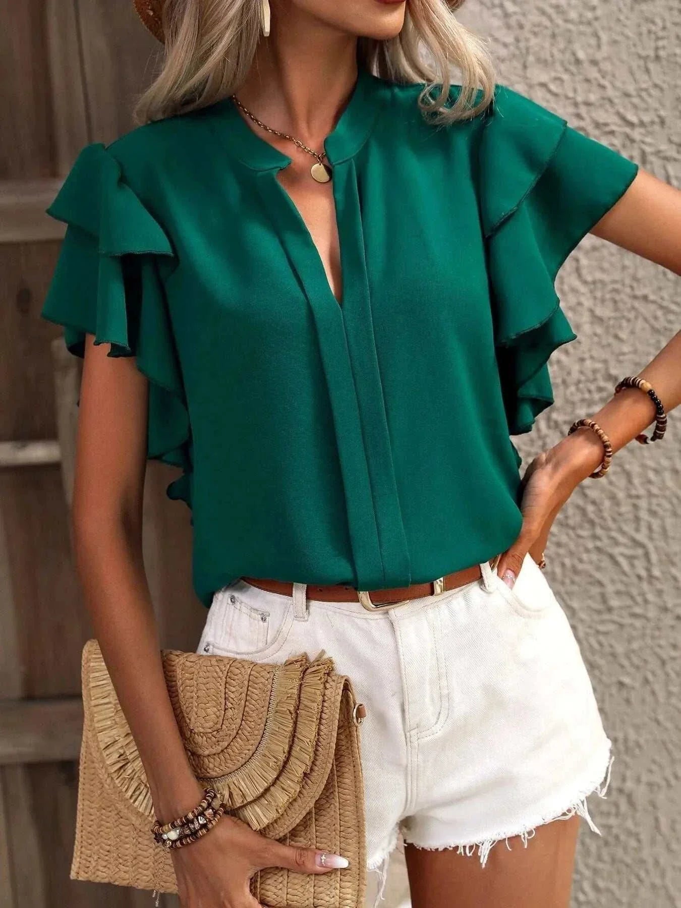 Green ruffle sleeve notched blouse paired with white shorts and a straw clutch bag