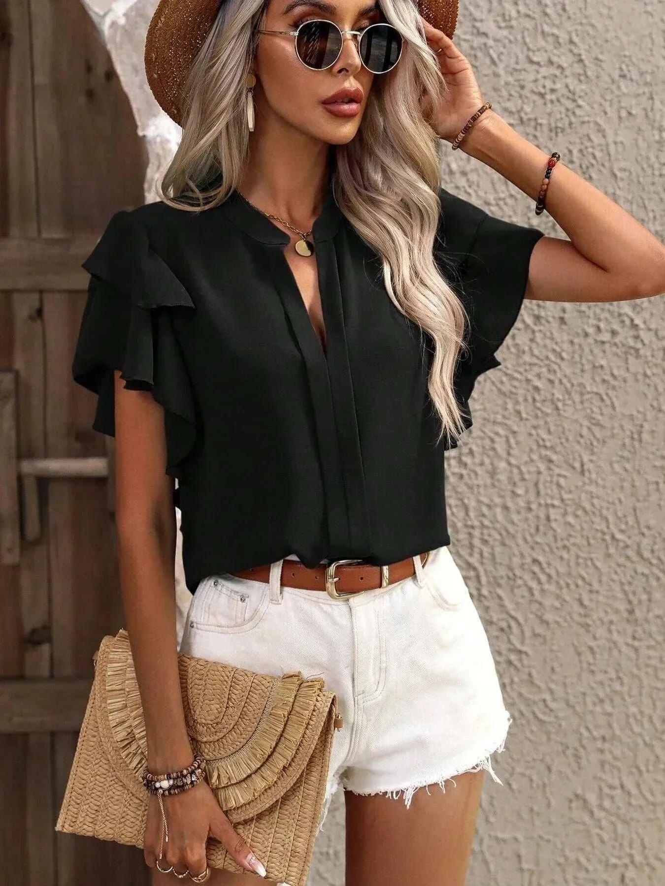 Black ruffle sleeve notched blouse made of 100% polyester with no stretch, styled with white shorts and accessories.