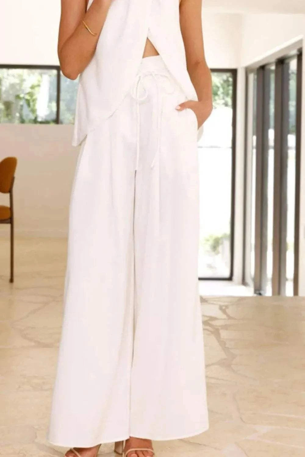 White halter neck top and wide leg pants set with tied waist and pockets, made of polyester and spandex, styled in a modern, relaxed fit.