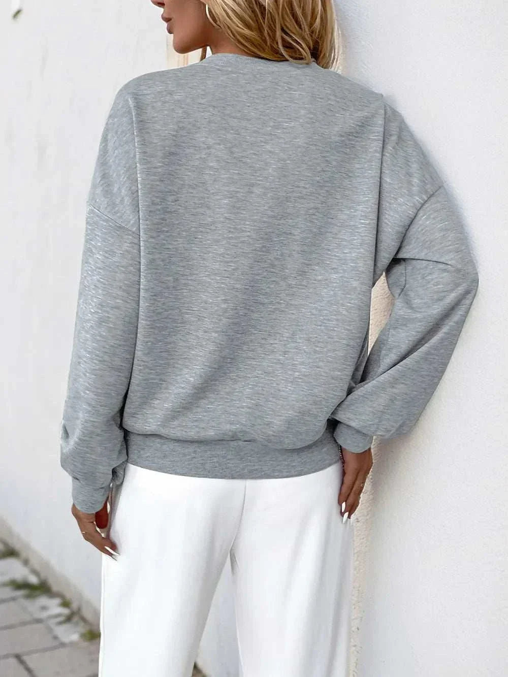 Back view of a woman wearing a gray long sleeve sweatshirt with a round neck and pearl cutout details, paired with