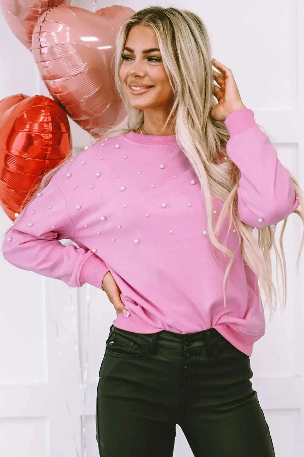 Woman wearing pink pearl round neck dropped shoulder sweatshirt with black pants and heart-shaped balloons