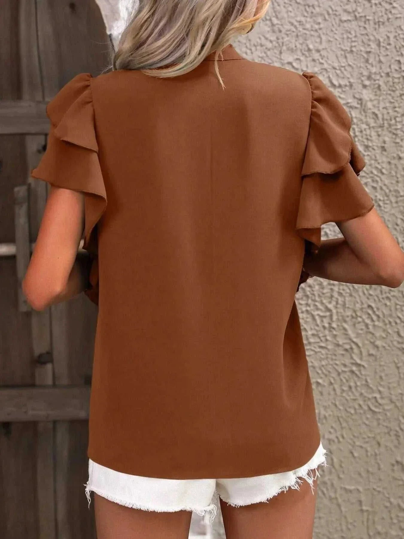 Back view of a brown ruffle sleeve notched blouse made of 100% polyester paired with white frayed shorts