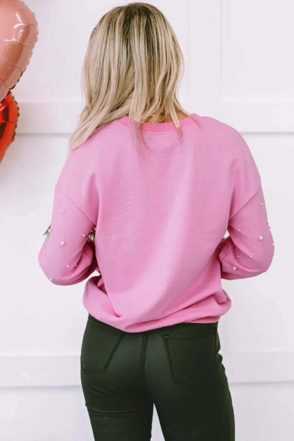 Pink pearl-adorned round neck dropped shoulder sweatshirt worn by woman from the back.