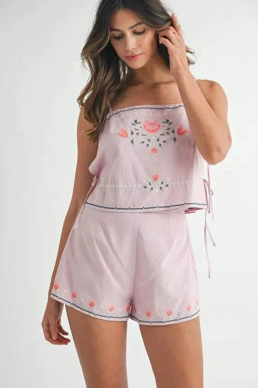 Woman wearing a light pink embroidered crop top and matching shorts set with floral designs and side ties.