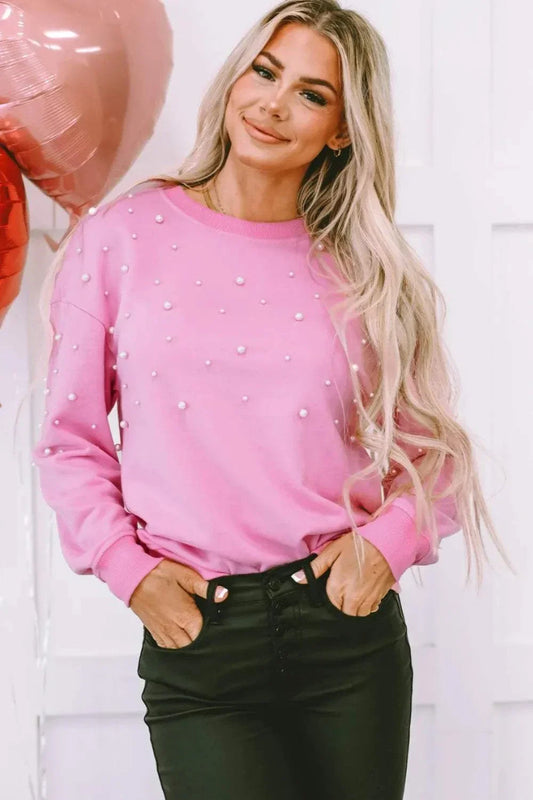 Woman wearing pink pearl-embellished round neck dropped shoulder sweatshirt with black pants