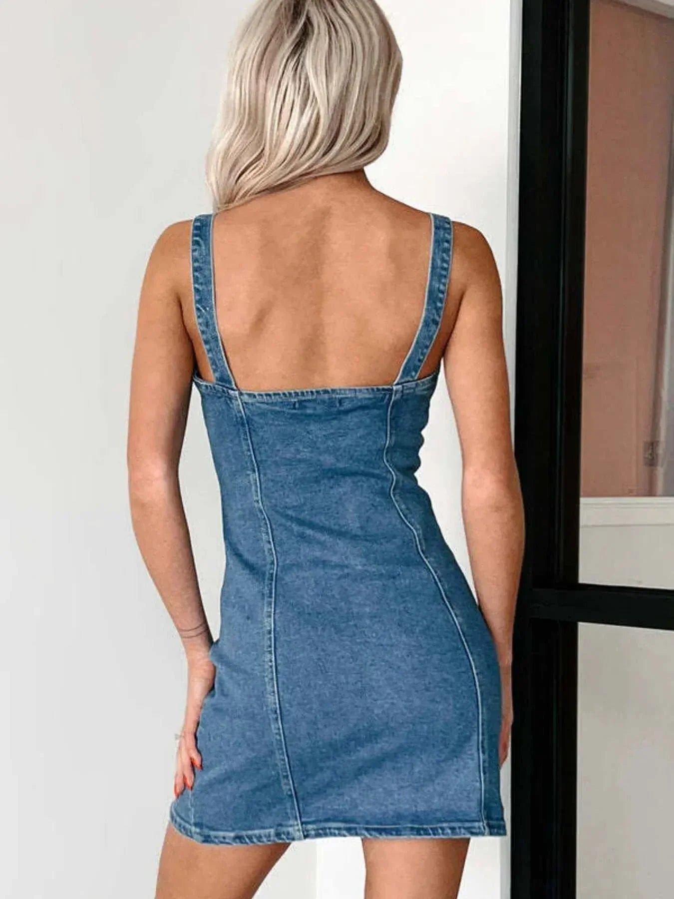 Back view of a woman wearing a button front sweetheart neck denim mini dress with wide straps.
